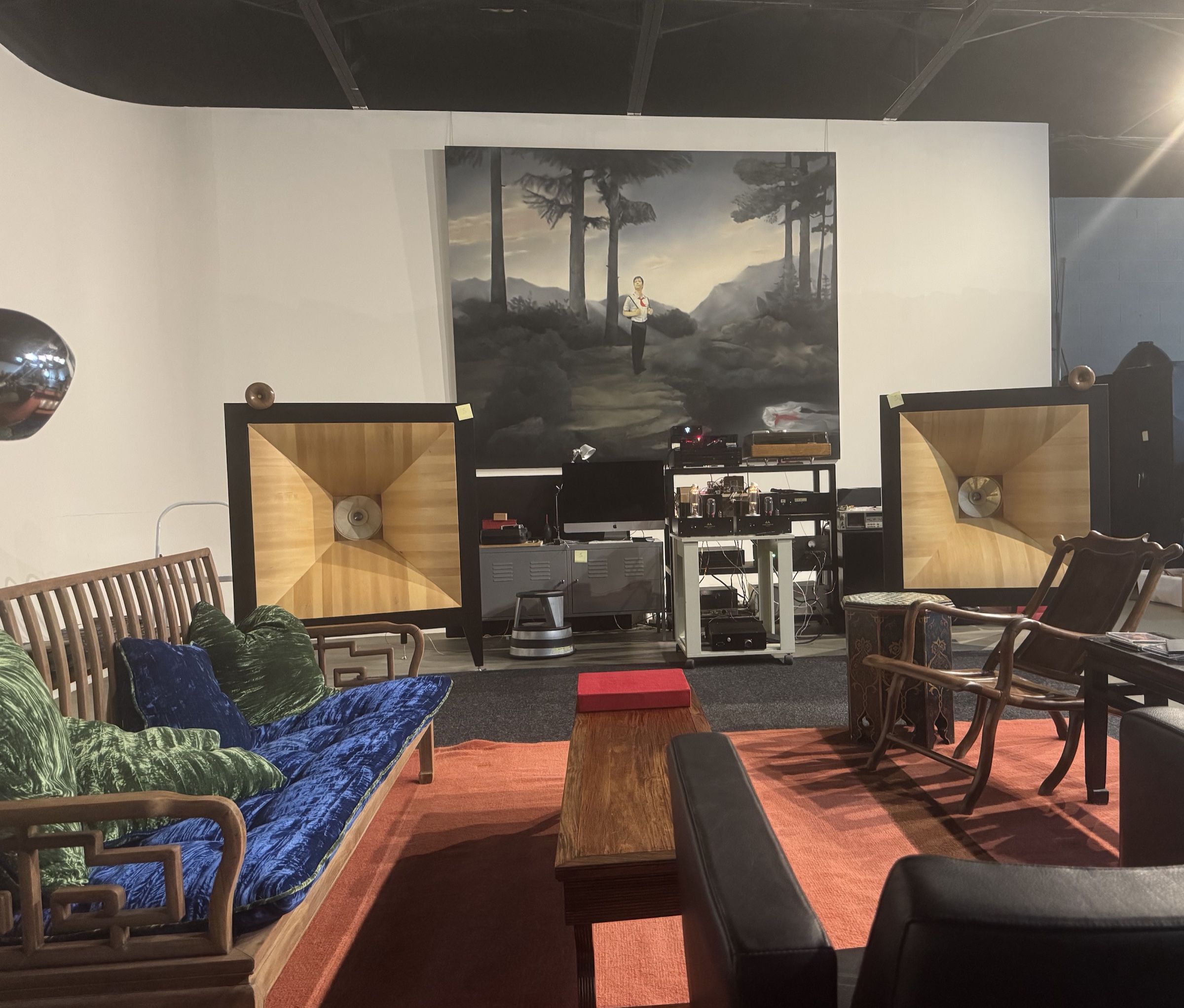 A pair of Semrad Audio horn speakers with light wood horn mouths in dark cabinets, in a showroom with a green velvet sofa, tube amplification, and a large landscape painting.